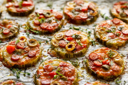 grilled-zucchini-slices-with-addition-of-mozzarella-cheese-sausage-green-olives-capers-and-herbs-on-white-baking-paper-close-up-delicious-appetizer-zucchini-pizza-bites